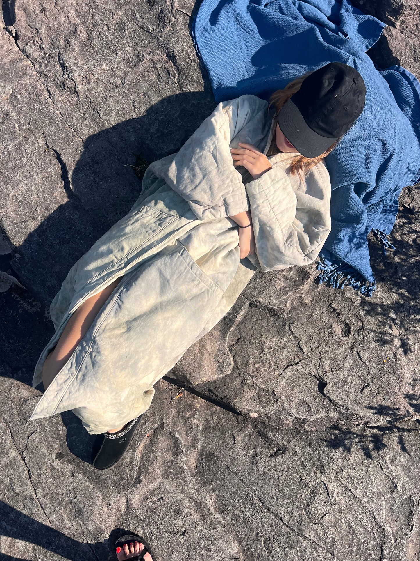 Model wearing long kimono coat lounging on a rock by the river.