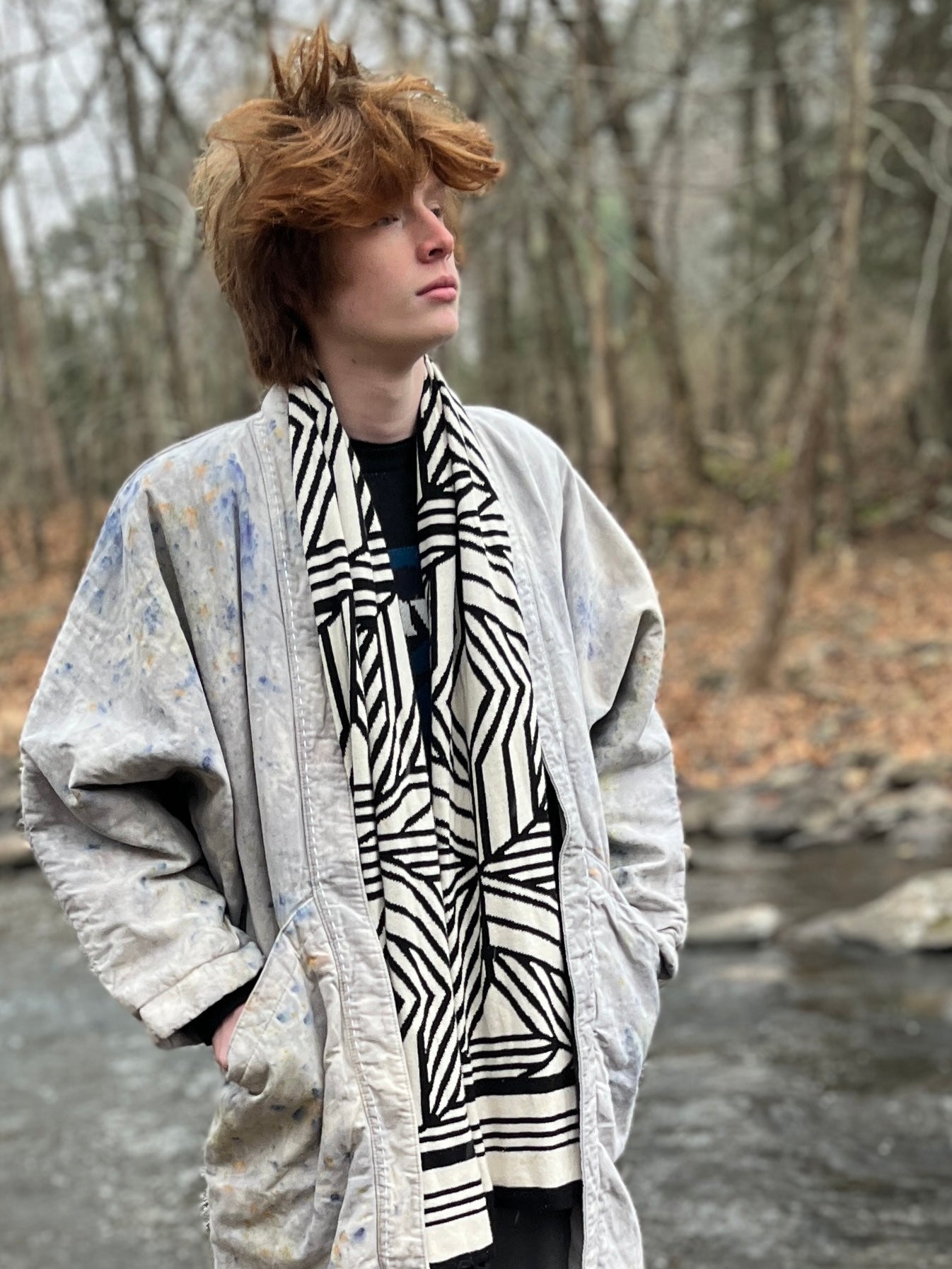 Person wearing a patterned scarf and light-colored coat in a forest setting
