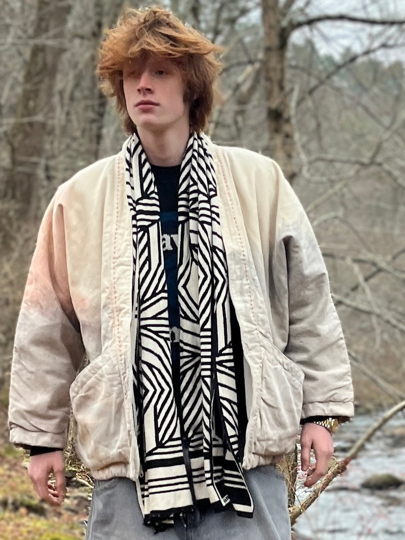 Person wearing a patterned scarf and light jacket in a forest setting